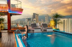 A rooftop pool area with a view of a city skyline, including high-rise buildings and mountains in the background. - MERCY EMERALD HOTEL (Da Nang)