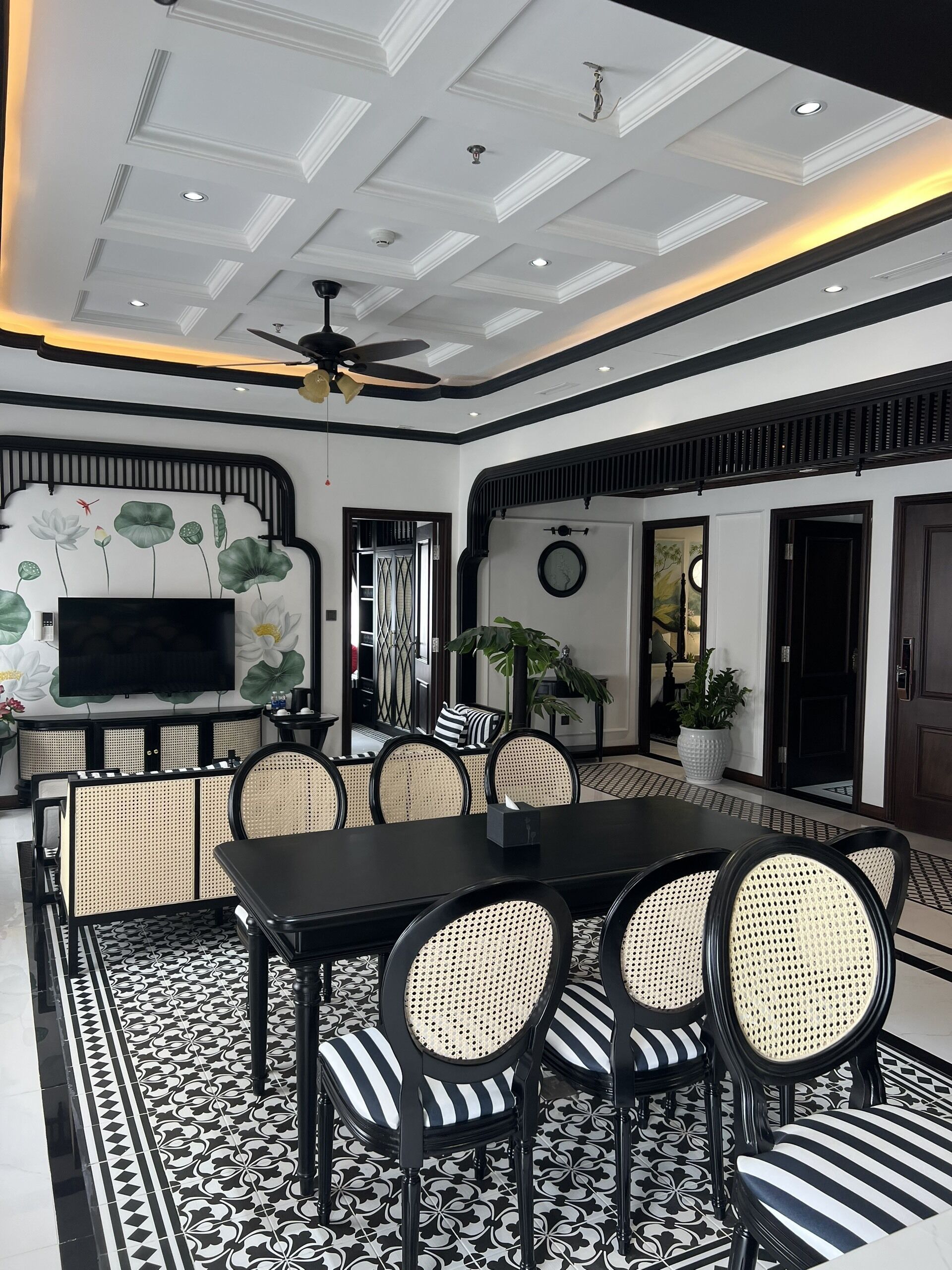 A dining area with a black table and chairs, a ceiling fan, and a decorative wall with a lotus motif.