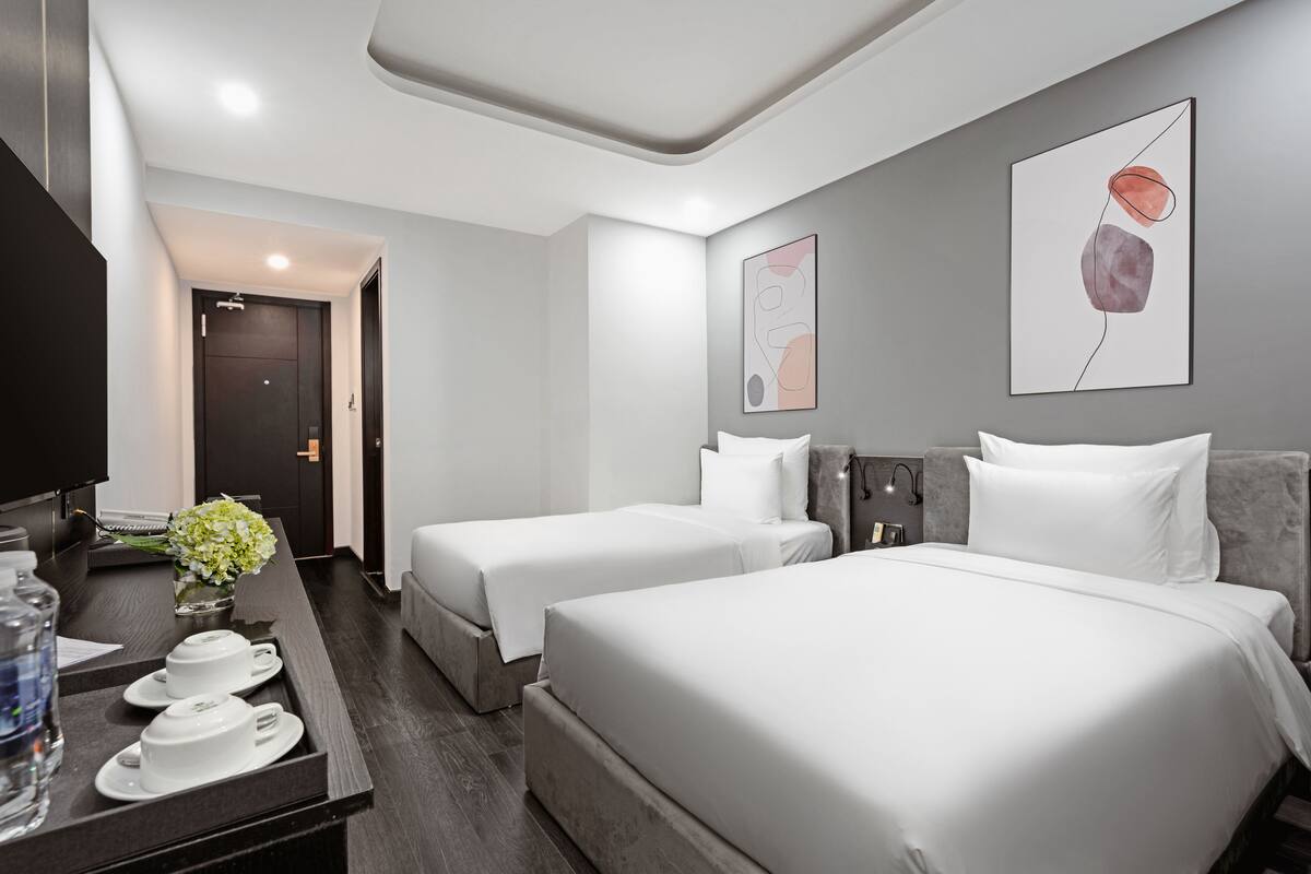A hotel room with two beds, a desk with a vase of flowers, and artwork on the walls.