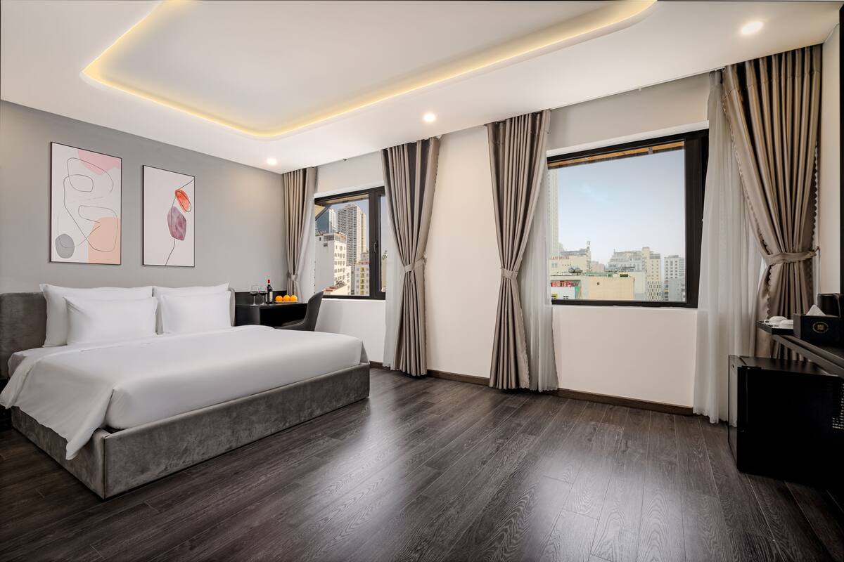 A modern hotel room with a large bed, a city view, and a minimalist design.