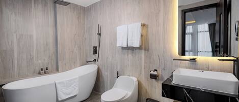A modern bathroom with a freestanding bathtub, a toilet, a sink, and a mirror.
