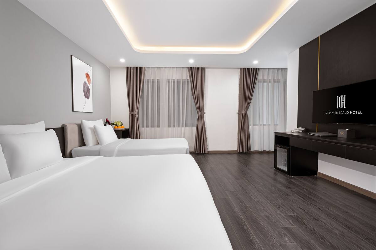 A modern hotel room with a large bed, a desk with a flat-screen TV, and a minibar.