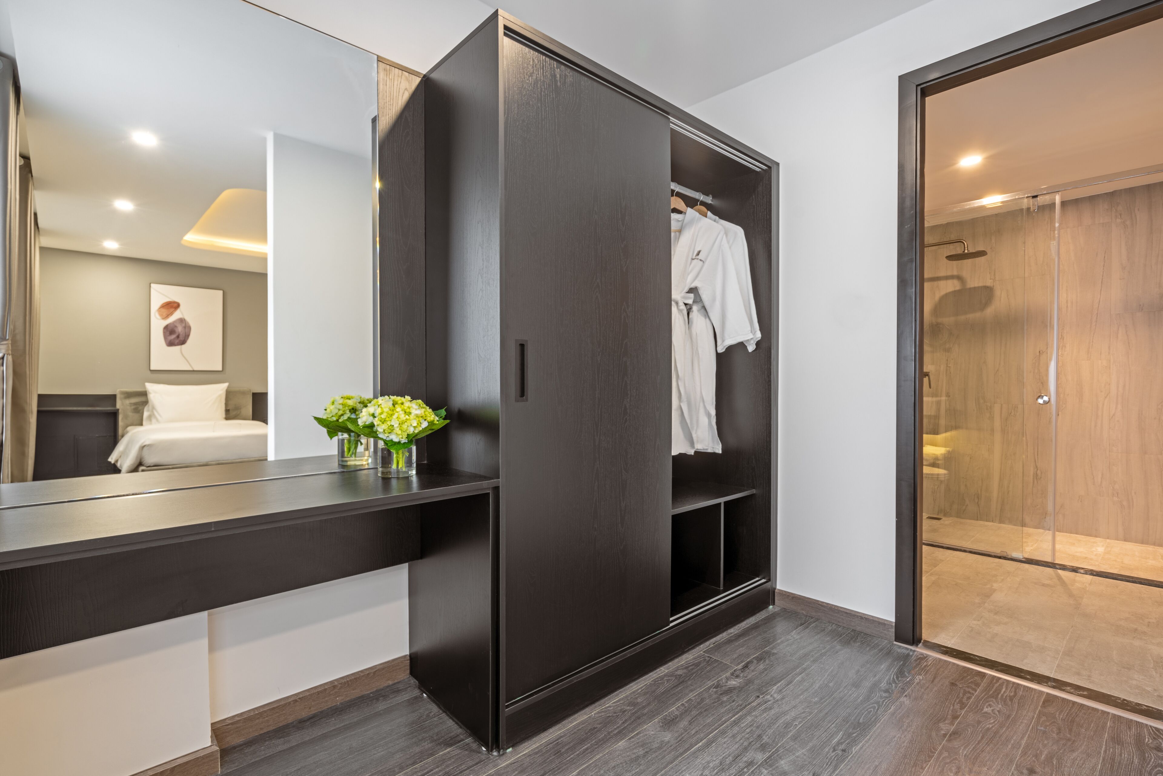 A modern bathroom with a dark wood wardrobe, a vanity with a mirror, and a shower area.