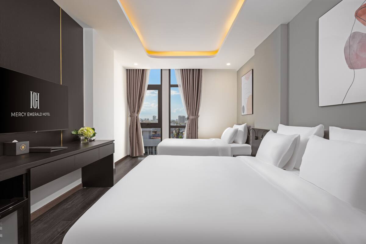 A modern hotel room with a large bed, a TV, and a desk with a flower vase.