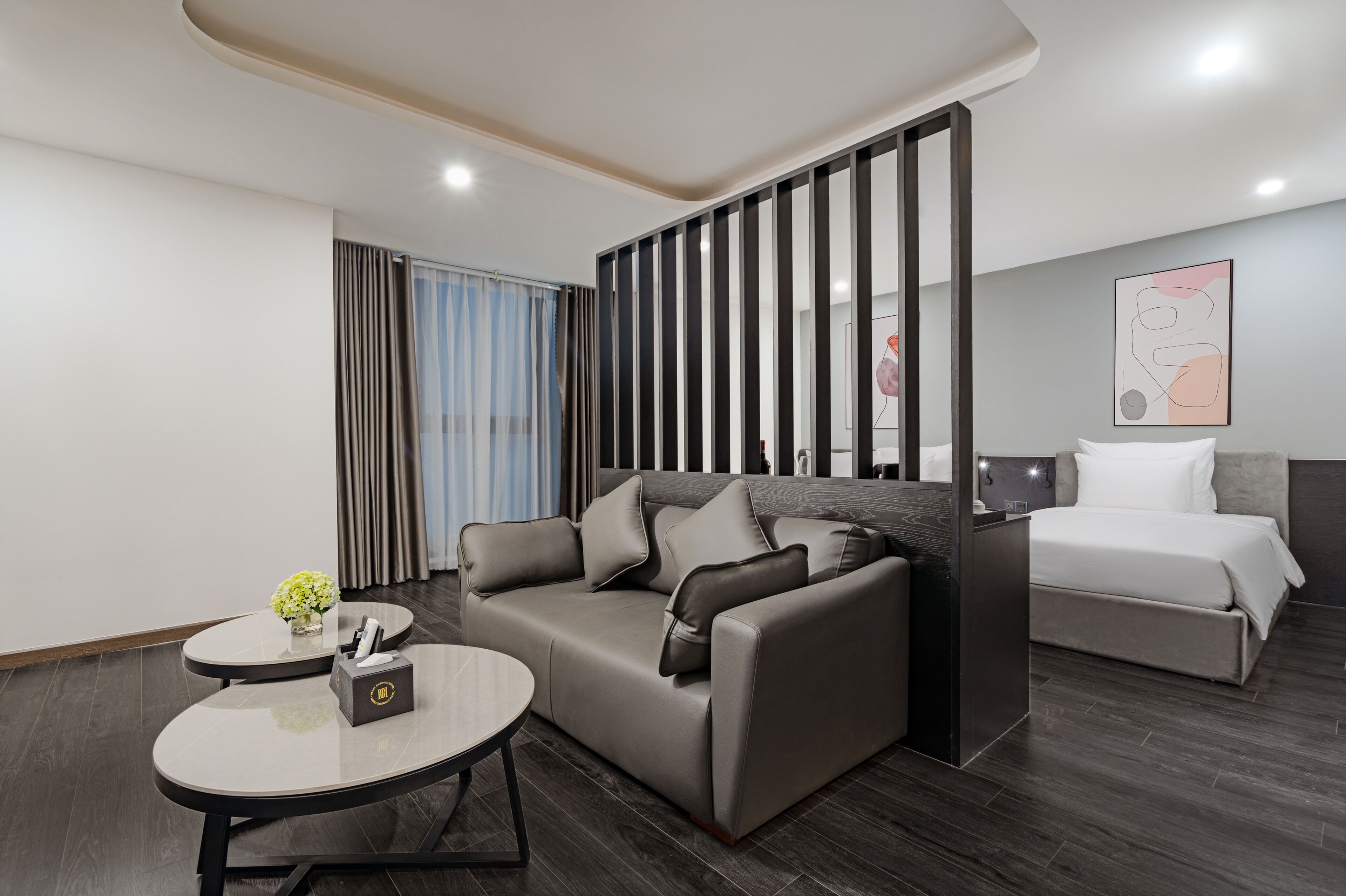 Una habitación de hotel moderna con sofá, una mesa redonda, una cama y un separador decorativo.