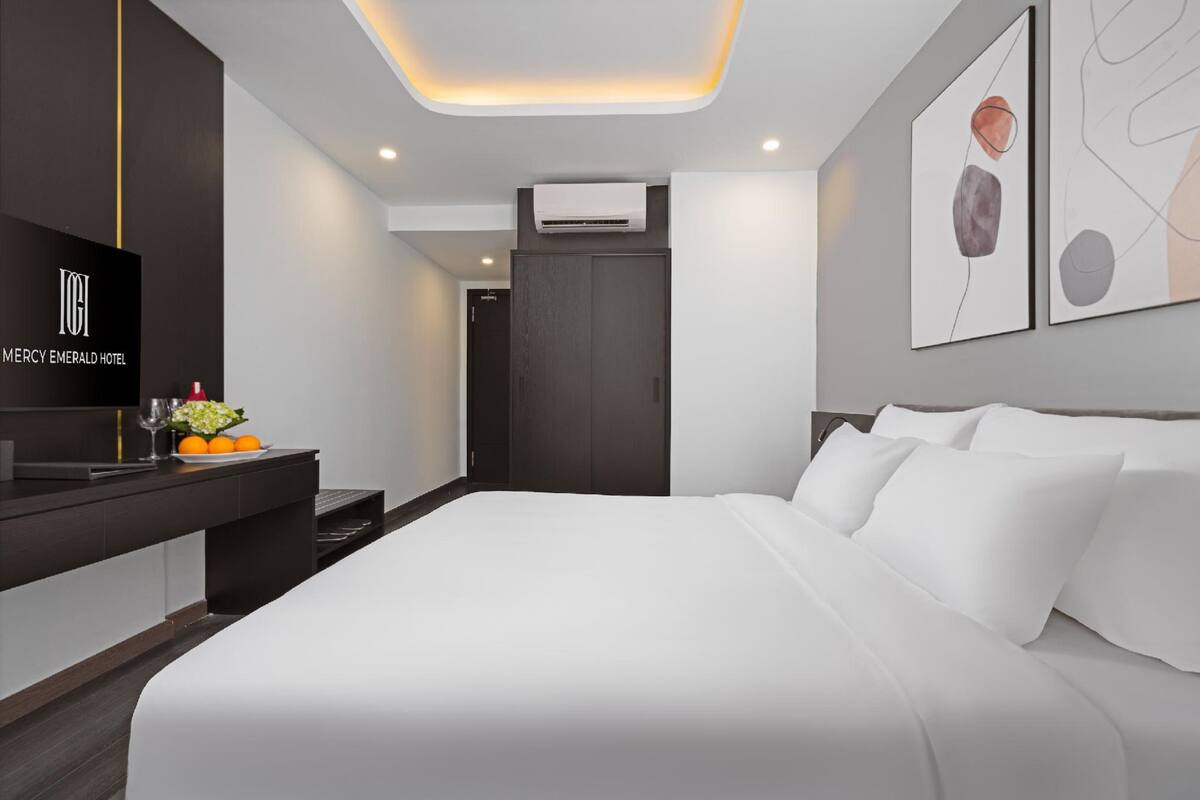 A modern hotel room with a large bed, a flat-screen TV, a desk with a vase of flowers, and artwork on the walls.