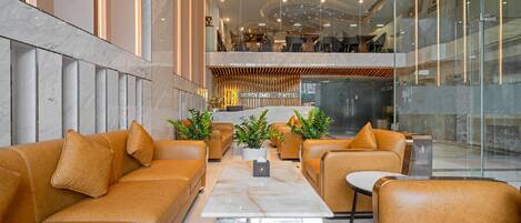 A modern hotel lobby with leather sofas, a marble coffee table, and potted plants.