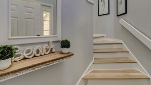A staircase with wooden steps and white railings, leading to a landing with a mirror and framed artwork. - SALT LIFE TREEHOUSE --BEAUTIFUL VIEWS! Huntington Villas (Hilton Head Island)