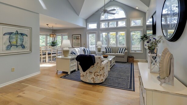 A spacious living room with a high ceiling, large windows, and a ceiling fan. - SALT LIFE TREEHOUSE --BEAUTIFUL VIEWS! Huntington Villas (Hilton Head Island)