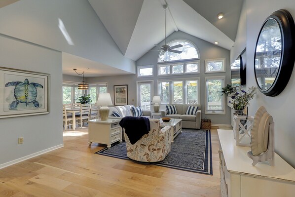 Relax in this spacious living room with a high ceiling and large skylight, featuring a comfortable sofa set and decorative rug.