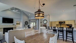 A modern living room with a wooden dining table, white chairs, a sofa, and a fireplace. - SALT LIFE TREEHOUSE --BEAUTIFUL VIEWS! Huntington Villas (Hilton Head Island)