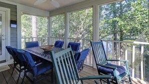 A covered outdoor dining area with a table and chairs, a ceiling fan, and large windows overlooking a wooded area. - SALT LIFE TREEHOUSE --BEAUTIFUL VIEWS! Huntington Villas (Hilton Head Island)