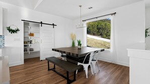 Una cocina moderna con una mesa de madera, sillas blancas y vistas a zonas verdes.