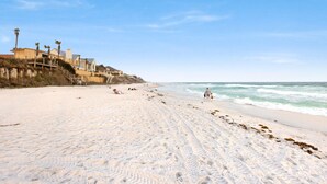 Una playa arenosa con huellas que conducen al agua, una escalera de madera y un edificio de varios pisos.