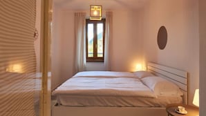 Ein Hotelzimmer mit Bett, Nachttisch mit Lampe, Fenster mit Vorhängen und einer Wandleuchte.