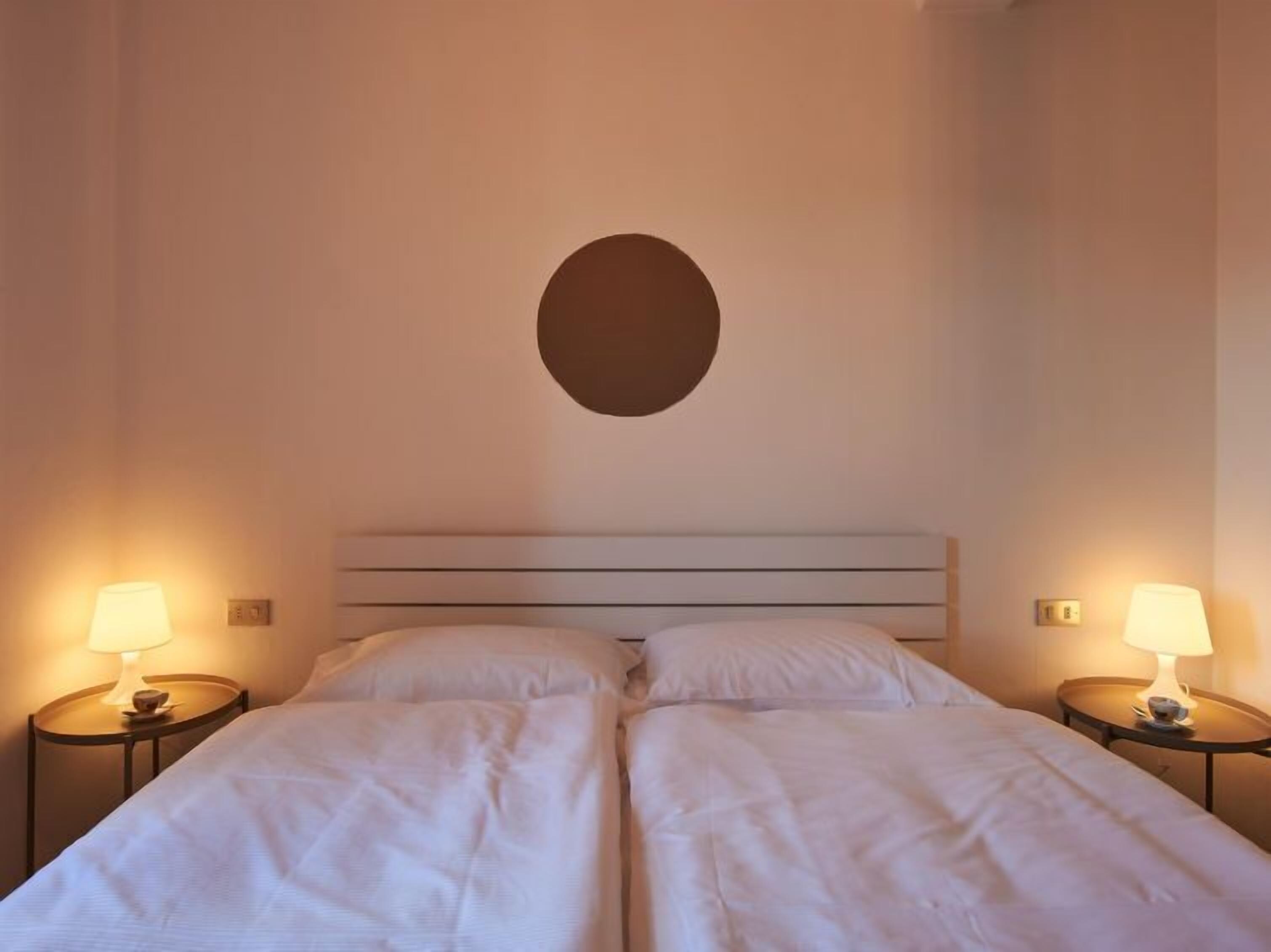 A hotel room with two beds, each with a nightstand and a lamp.