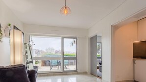 Een moderne woonkamer met een bank, een bijzettafeltje en een decoratieve fauteuil. Er is een groot raam met uitzicht op de omgeving.