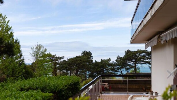 Een modern gebouw met een glazen balkon dat uitkijkt over een tuin en een waterpartij.