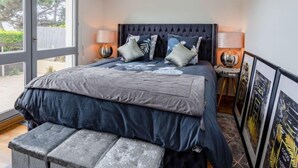 Een slaapkamer met een groot bed, twee bedlampen, een bankje en uitzicht op de omgeving.
