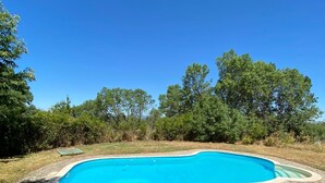 A rectangular swimming pool with a stone border, surrounded by grass and trees. - Hermosa Finca Rural (Navalmoral de bejar)