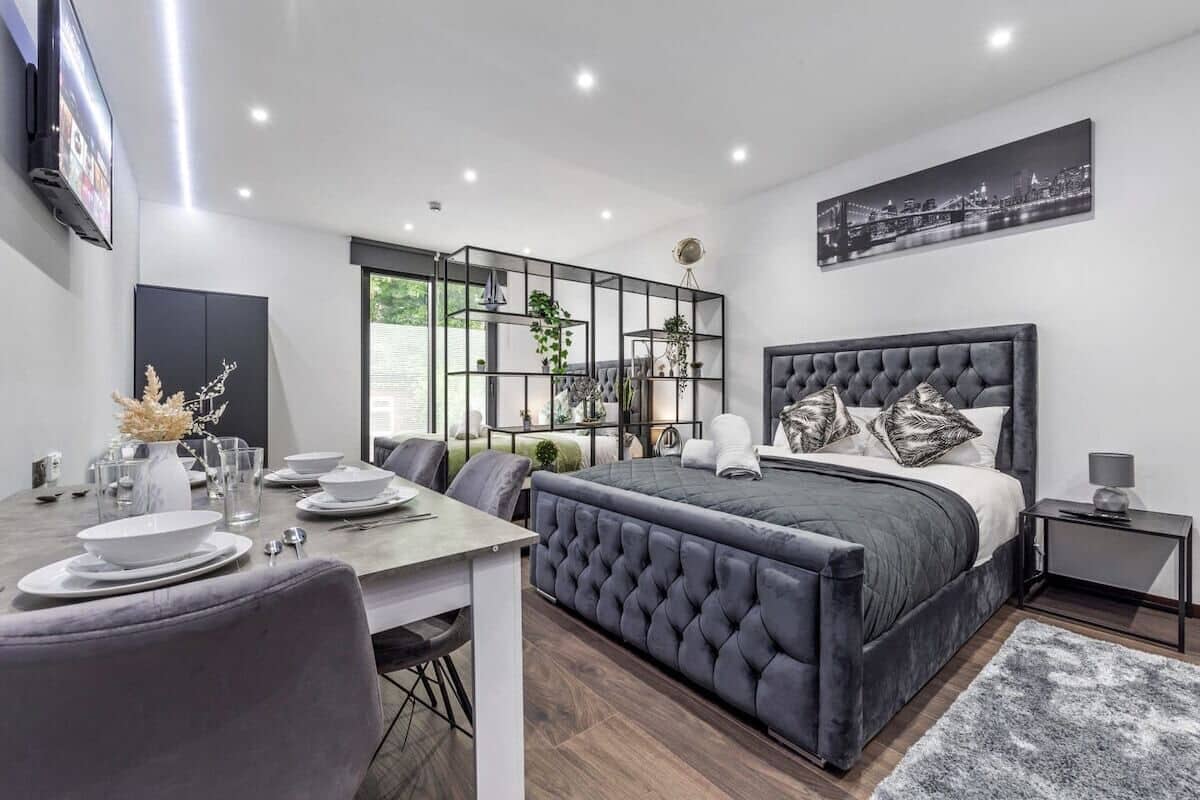 A modern bedroom with a large bed, a dining area with a table set for two, and a cityscape view.