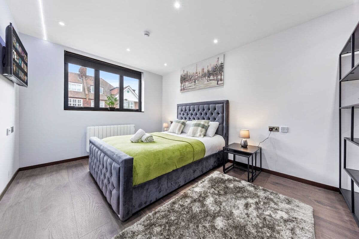 A modern bedroom with a large bed, a view of the outside through a window, and a small bedside table with a lamp.