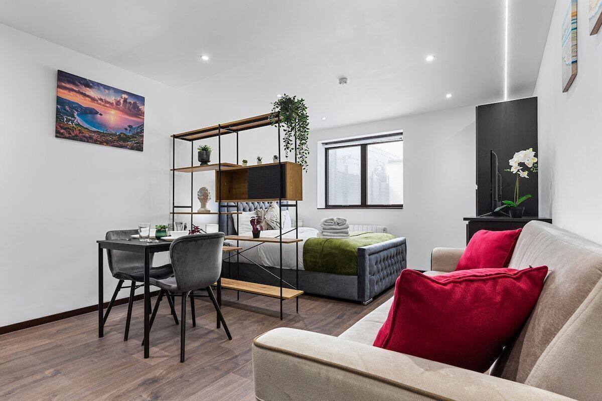 A modern living room with a sofa, a dining table with chairs, a bookshelf, and a large window.