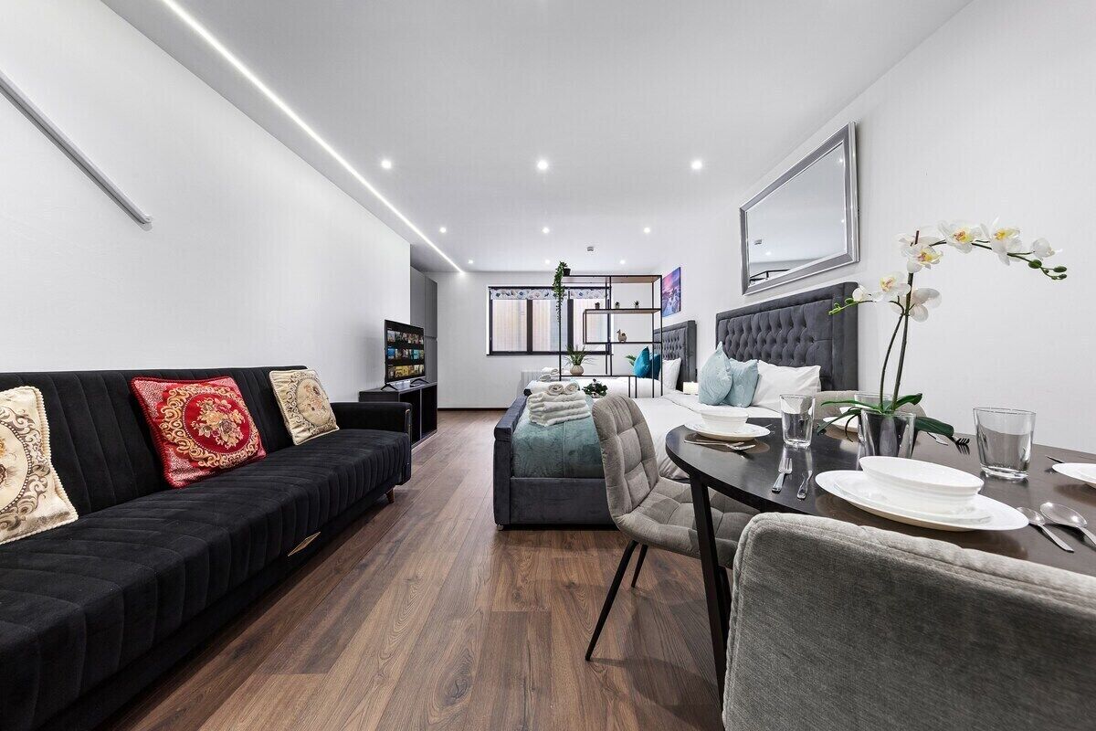 A modern living room with a black sofa, a dining table set for two, and a grey upholstered chair.