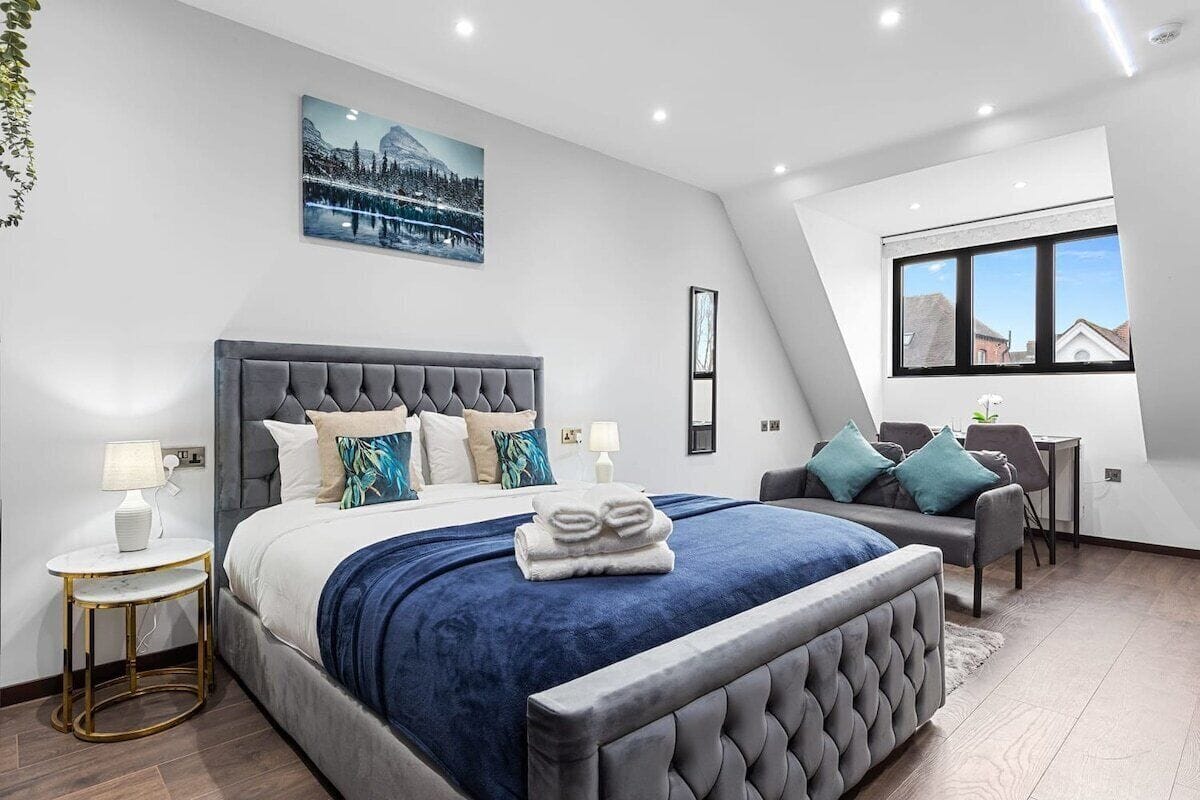 A modern bedroom with a large bed, a desk, and a view of the outside.