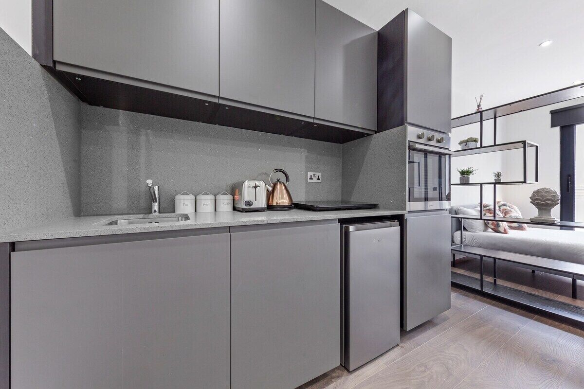 A modern kitchen with grey cabinetry, a built-in oven, and a coffee maker.
