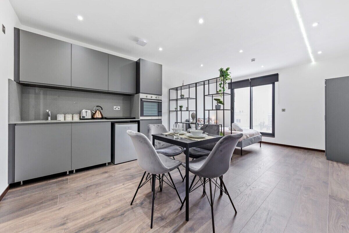 Une cuisine moderne avec des meubles gris, un coin repas comprenant une table et des chaises, et une grande fenêtre offrant une vue sur la ville.