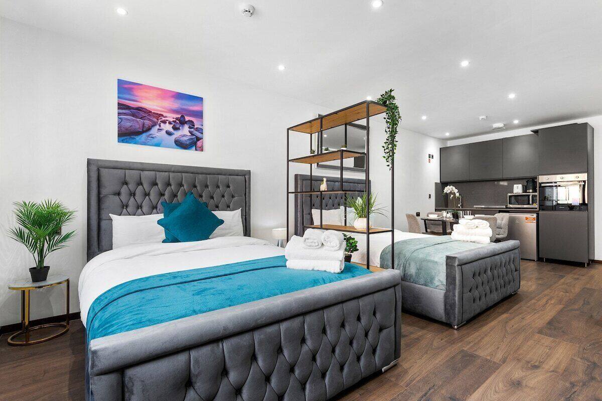 A modern hotel room with two beds, a kitchenette, and a painting on the wall.