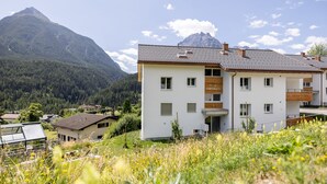 A modern two-story building with a flat roof, surrounded by lush greenery and mountains in the background.