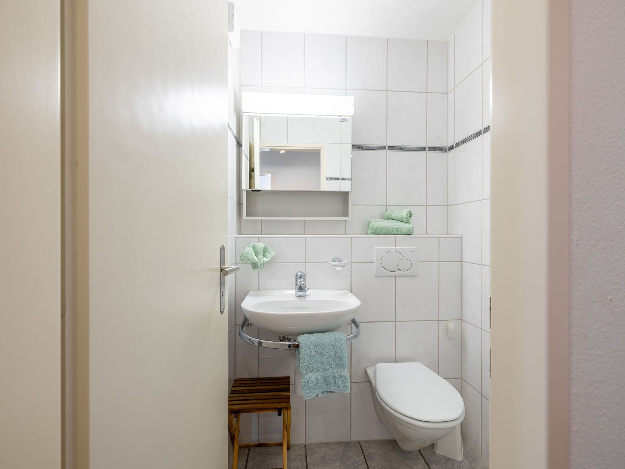 Un bagno piccolo con un lavandino bianco, un water e uno sgabello di legno.