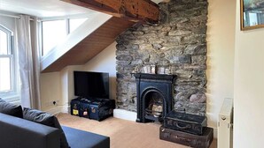 A cozy living room with a stone fireplace, wooden beams, a television, and luggage. - Tre@Westminster_Residence - Spacious Period Townhouse in Douglas with EV Charger (Douglas)