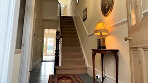 A hallway with a carpeted staircase, a wall-mounted lamp, and a door with a decorative plate. - Tre@Westminster_Residence - Spacious Period Townhouse in Douglas with EV Charger (Douglas)