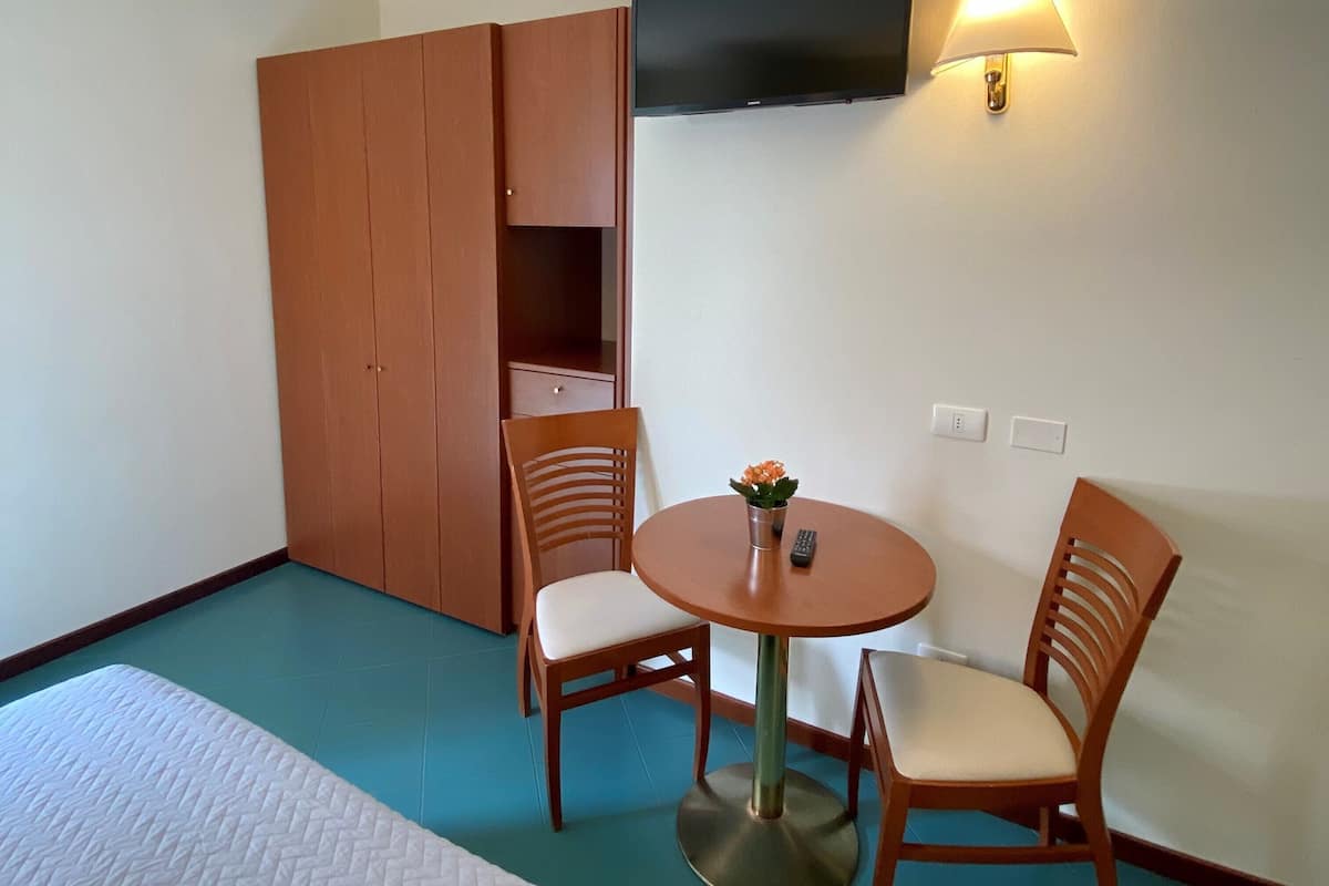 Una habitación con una cama, un armario de madera, un televisor montado en la pared y una mesa con dos sillas.