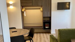 A modern living room with a dining area, a flat-screen TV mounted on the wall, and a built-in mini-fridge. - Hotel Pai (Torri del Benaco)