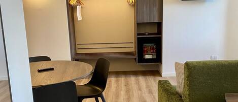 A modern living room with a dining area, a flat-screen TV mounted on the wall, and a built-in mini-fridge.