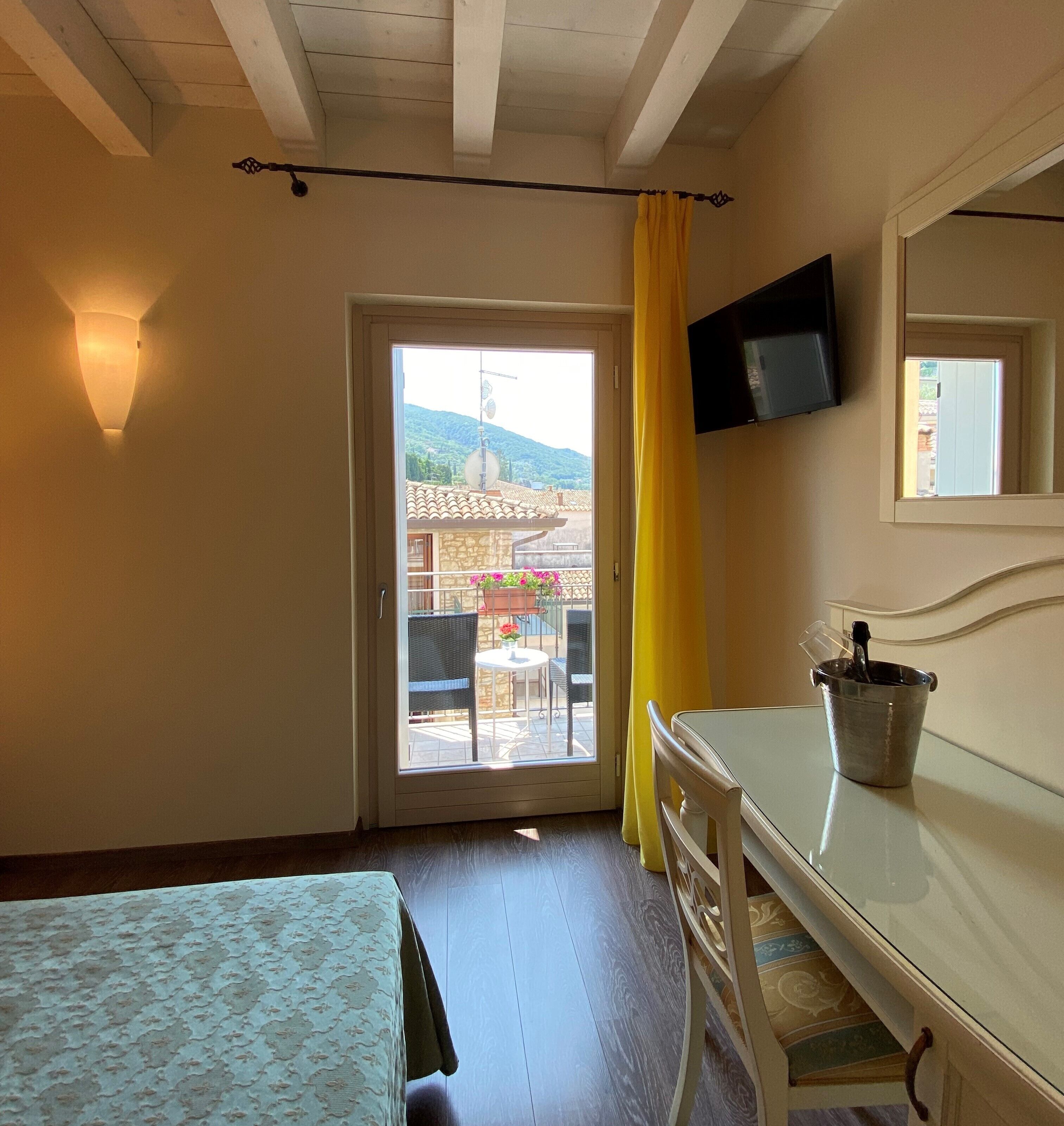 A room with a bed, a desk, a chair, a TV, and a window with a yellow curtain.