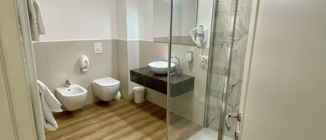 A modern bathroom with a glass shower enclosure, a bidet, a toilet, and a vanity with a sink.