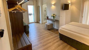 A hotel room with a wooden bench, a bed, a small table with a vase, and a TV mounted on the wall. - Hotel Pai (Torri del Benaco)