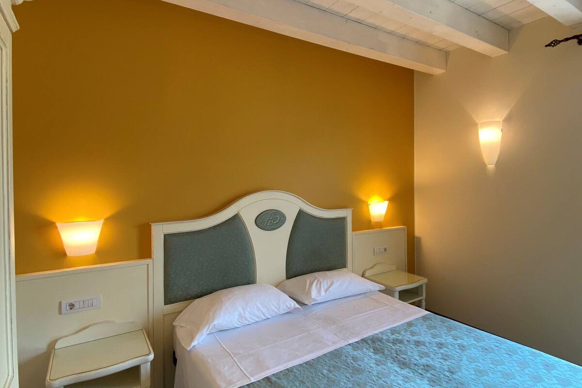 Una cama con cabecera blanca y dos mesitas de noche, cada una con una lámpara de pared.