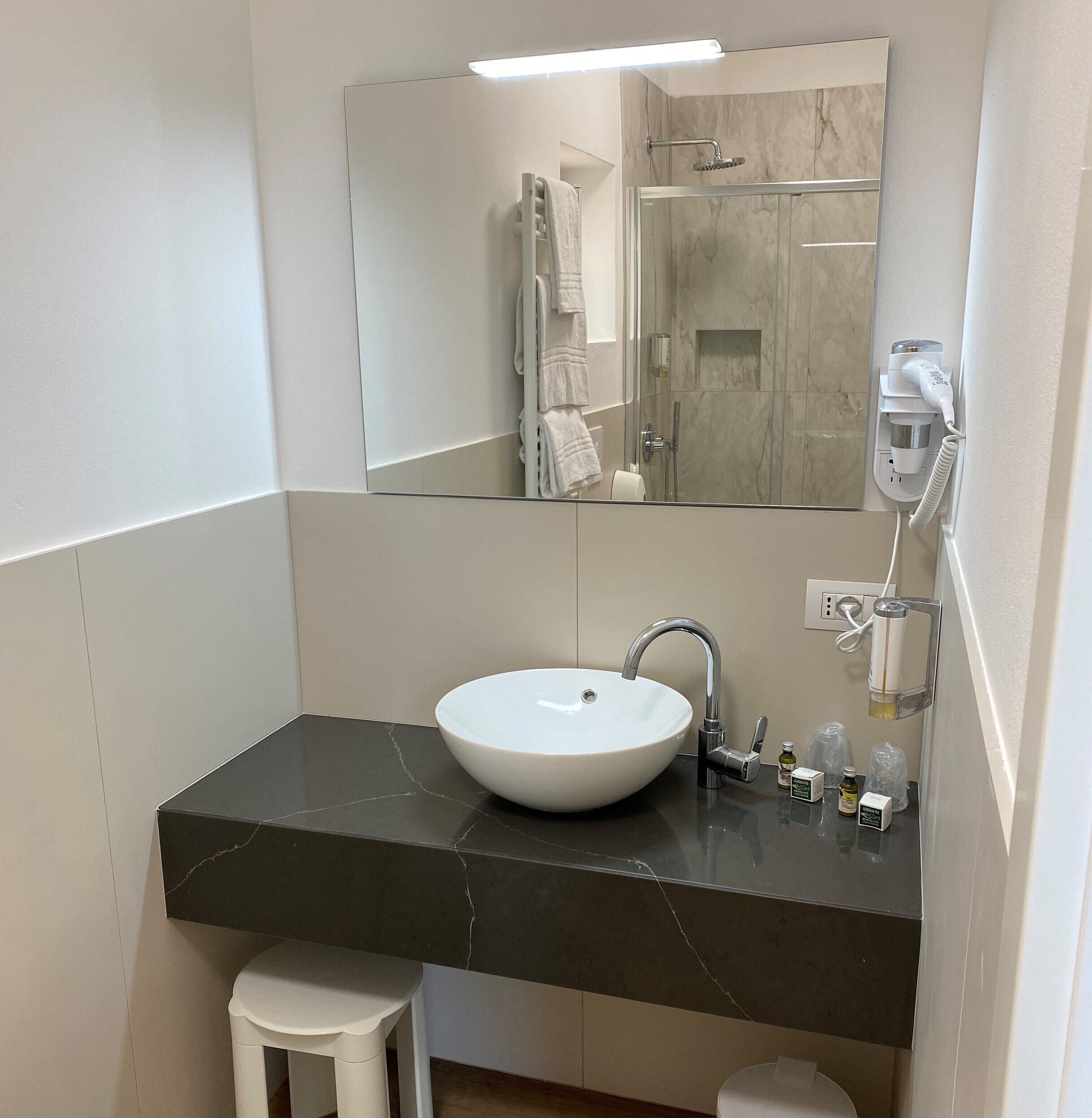 Une salle de bain moderne avec un lavabo blanc, un plan de toilette foncé et un grand miroir.