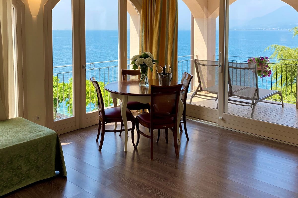 Un comedor con una mesa y sillas, un florero con flores y vista al mar a través de amplios ventanales.