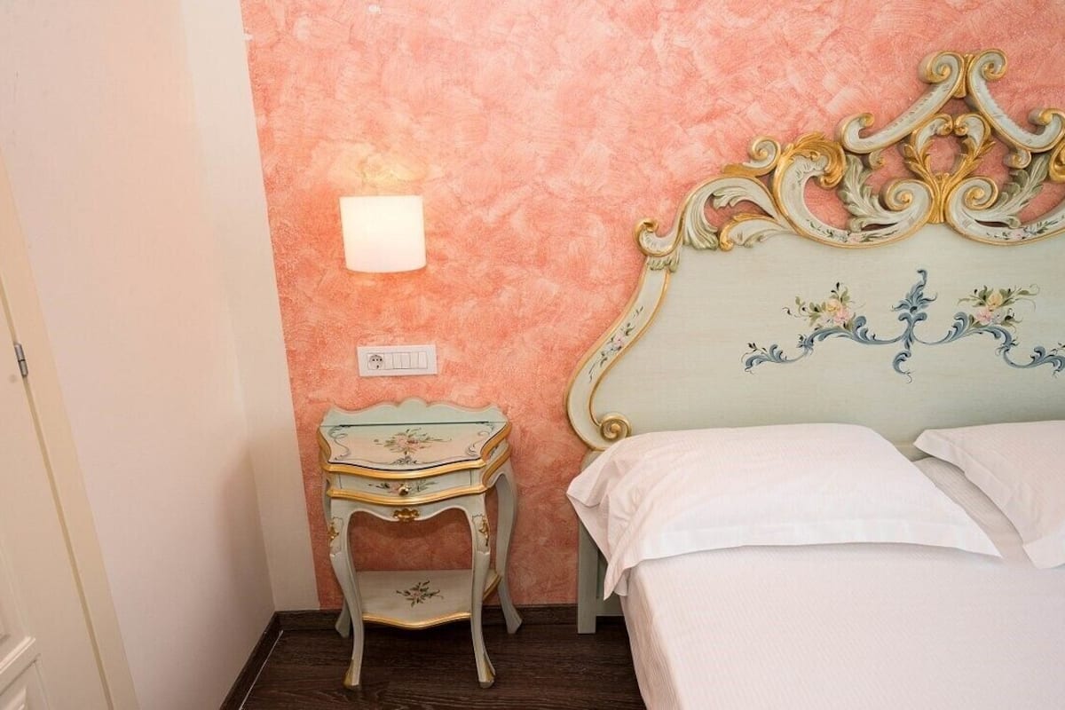 Un dormitorio con una cama, una mesita de noche, una lámpara de pared y un enchufe.