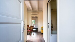 A narrow hallway with a wooden floor, a dining area with a table and chairs, and a yellow sofa. - Hotel Pai (Torri del Benaco)