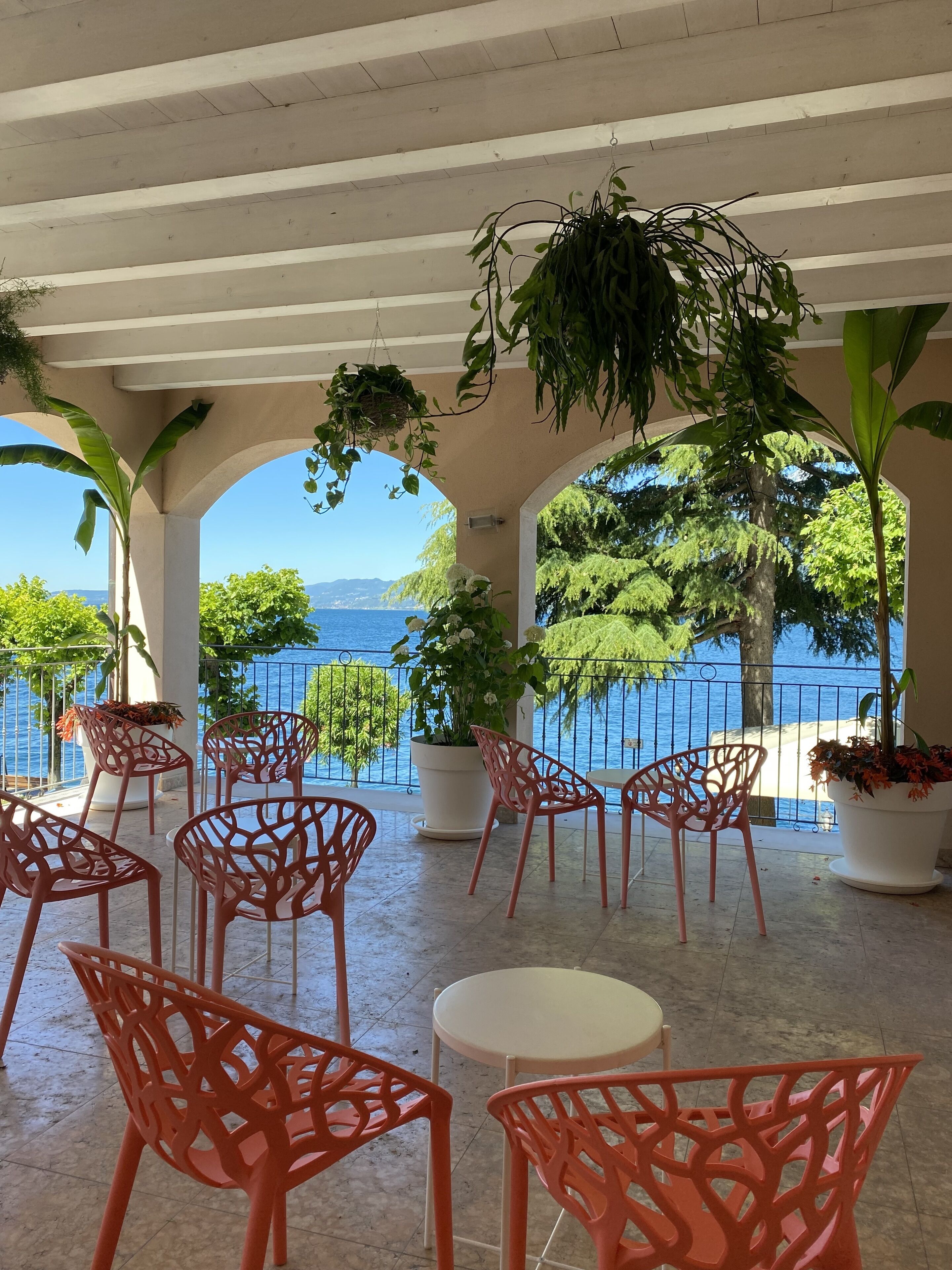 Eine Terrasse mit roten Stühlen und Topfpflanzen mit Blick auf ein Gewässer und Grünflächen.