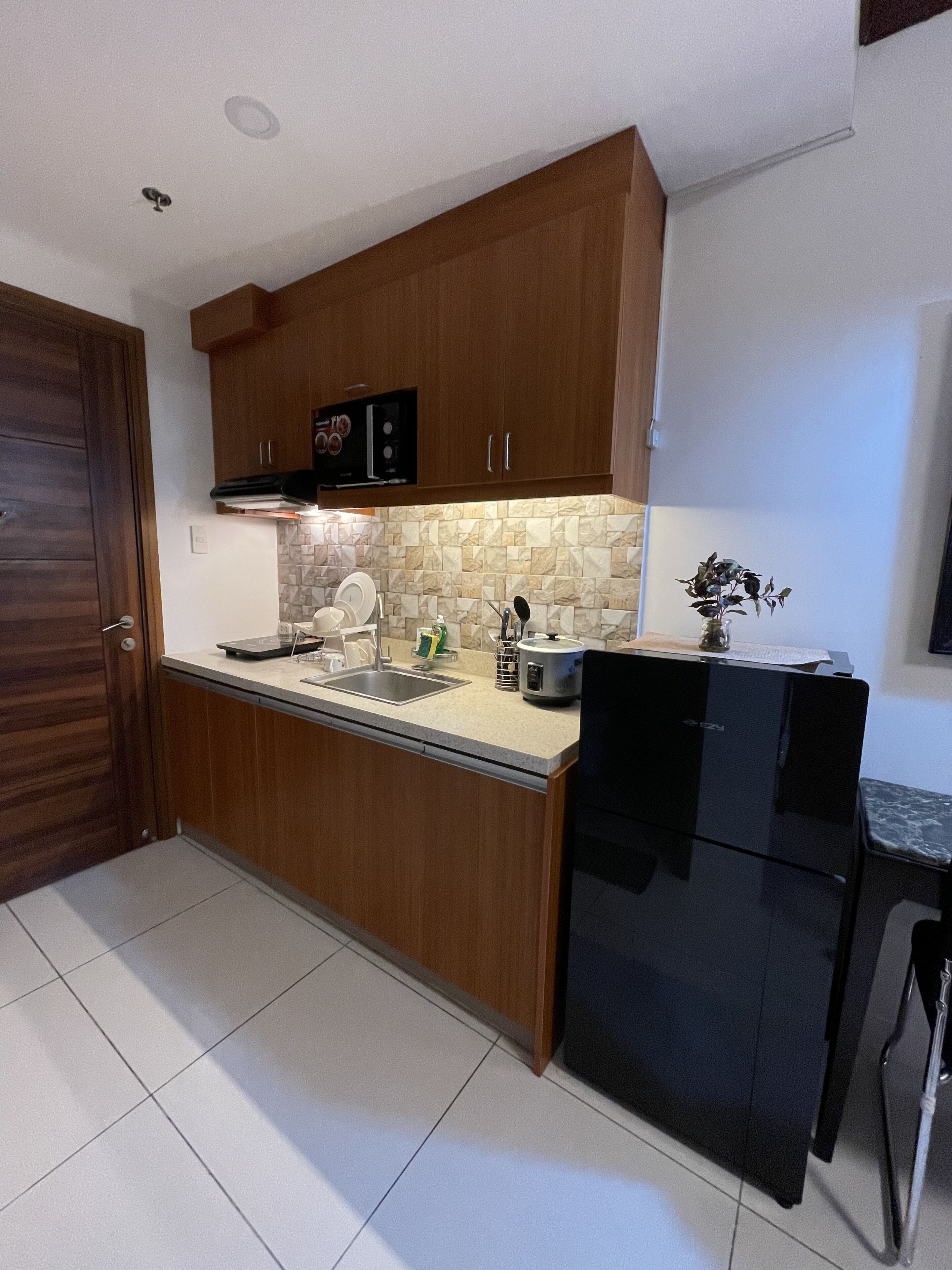 A kitchen with wooden cabinets, a black refrigerator, a tiled backsplash, and a countertop with various kitchen items.