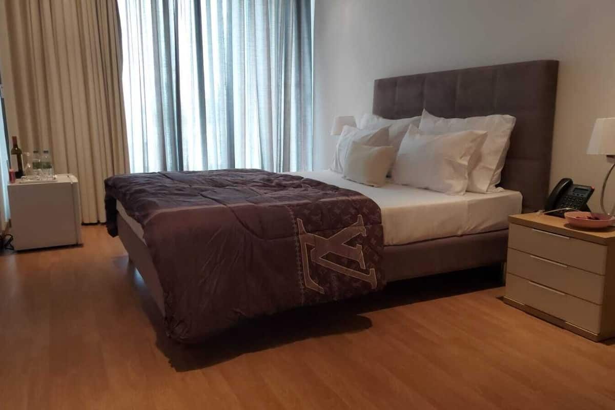 A hotel room with a bed, bedside table, lamp, and a window with curtains.